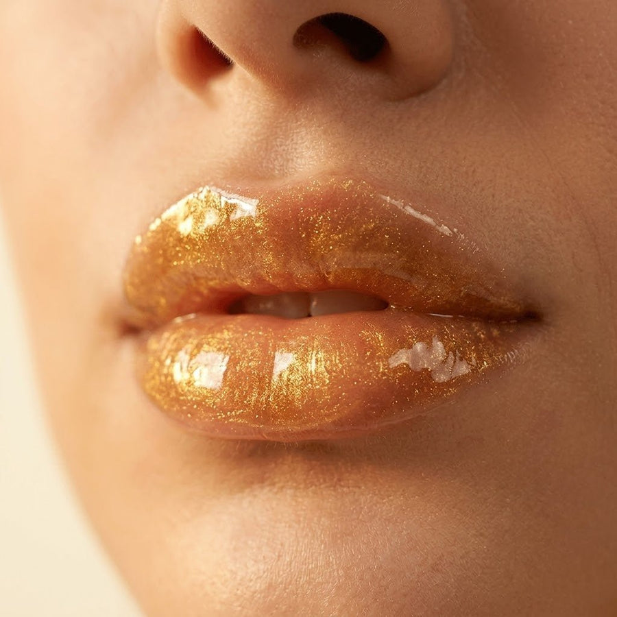 Close-up of lips with a gold lip gloss on a neutral background